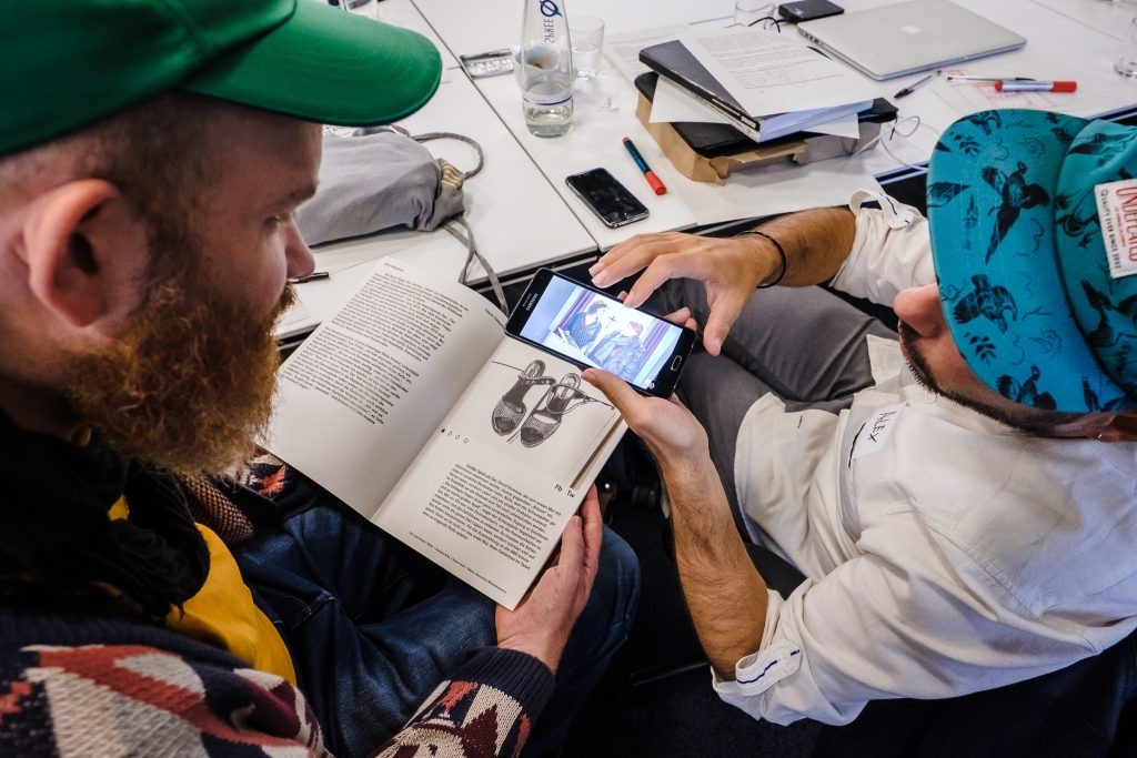 Zwei junge Männer schauen auf ein Smartphone, auf dem die App des Deaf Magazine aufgerufen ist.