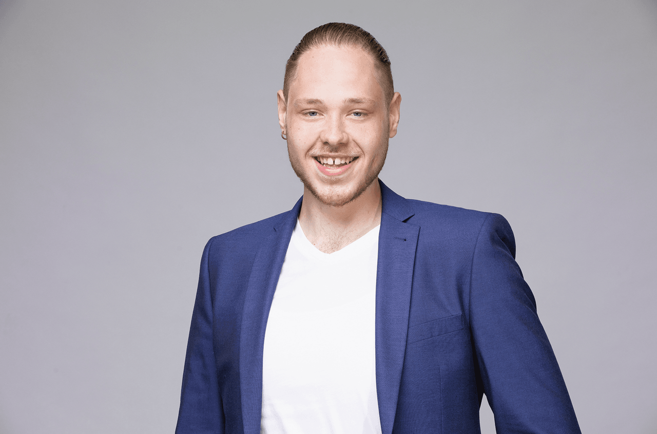 Nils Bollenbach mit weißem Shirt und blauem Blazer vor grauem Hintergrund