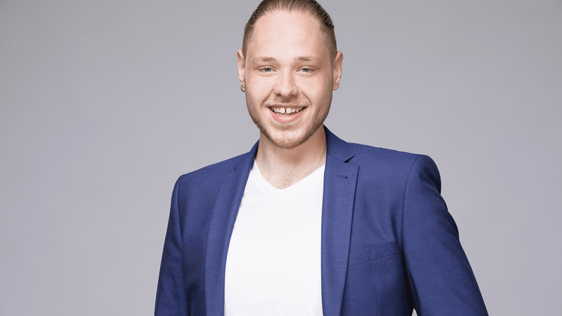 Nils Bollenbach mit weißem Shirt und blauem Blazer vor grauem Hintergrund