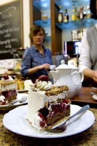 Ein Stück Kirsch-Krokant-Torte und im Hintergrund Sopie-Ann Bathe, die im Integrationsunternehmen Café Anker-Villa arbeitet.