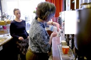 Lisa Kübler (links) schaut Ann-Sophie Bathe (rechts) dabei zu, wie sie Milch in den Tank einer großen Kaffeemaschine füllt.