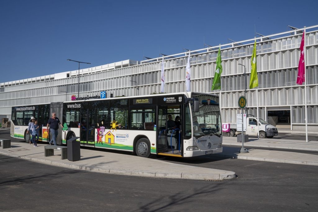Ein Shuttlebus an einem Bussteig, im Hintergrund ein großes Parkhaus. Foto: BUGA Heilbronn 2019 GmbH