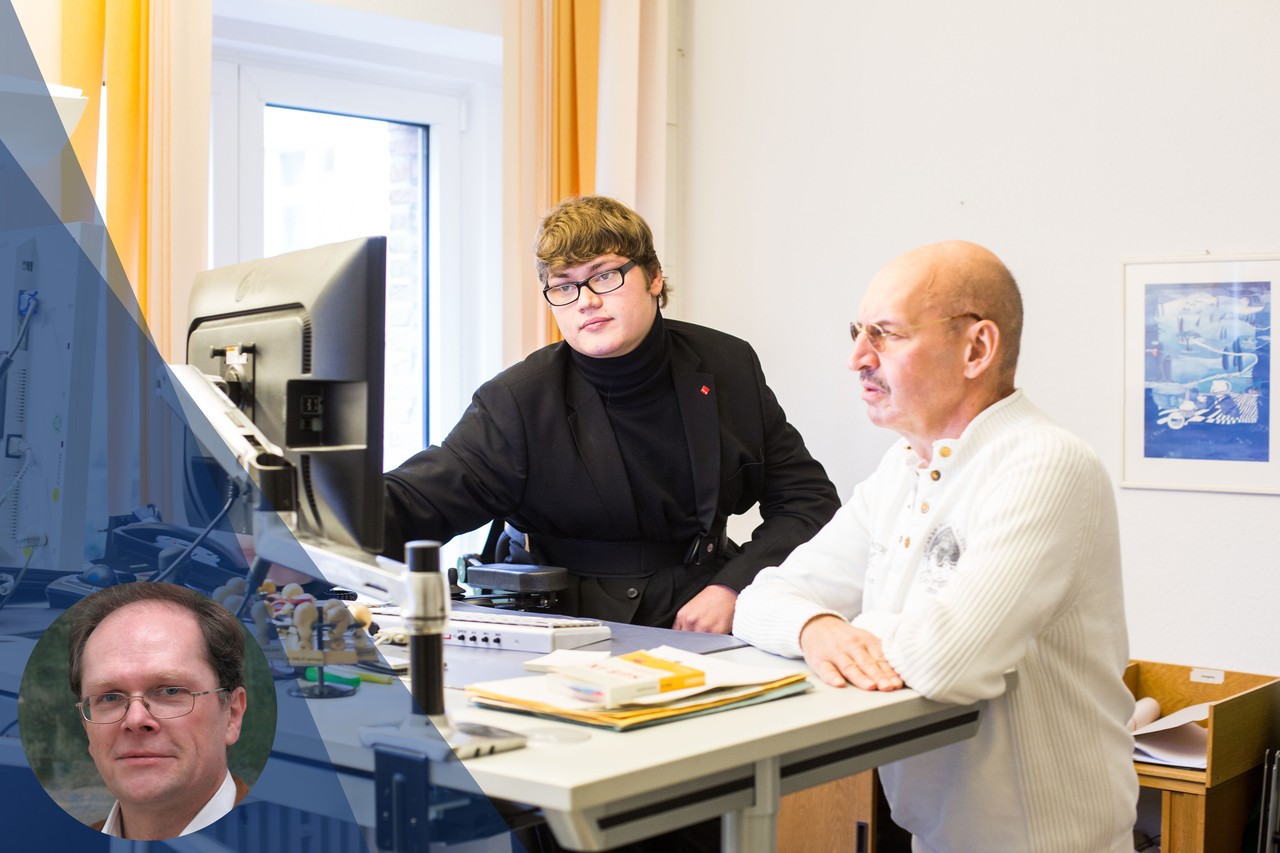 Ein Mitarbeiter mit Schwerbehinderung an seinem Büro-Arbeitsplatz, zusammen mit einem Kollegen.