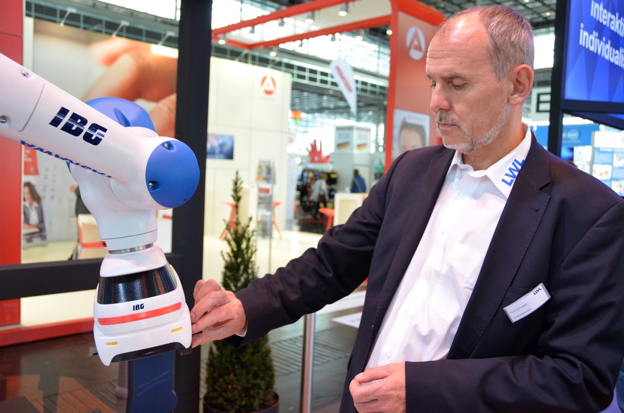 Frank Schrapper bedient gerade den Roboterarm und montiert ein Teil an einem Miniaturauto, das von dem Arm geführt wird.