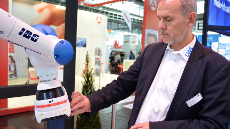 Frank Schrapper bedient gerade den Roboterarm und montiert ein Teil an einem Miniaturauto, das von dem Arm geführt wird.