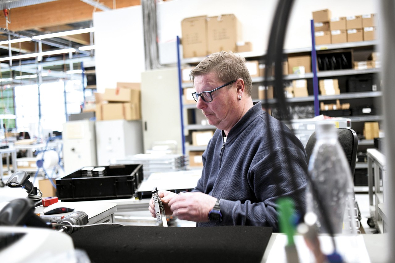 Ein Mitarbeiter der AfB sitzt in der Lagerhalle des Unternehmens an seinem Werktisch bearbeitet und konzentriert ein Computer-Bauteil, das er in der Hand hält.
