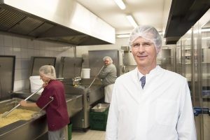 Bestfood-Chef Jürgen Groth steht mit Schutzhaube und Kittel in seiner Großküche.