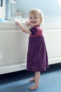 Laura, die zweite Tochter der Brunners, in einem selbstgenähten Kleidchen; sie lacht in die Kamera. 