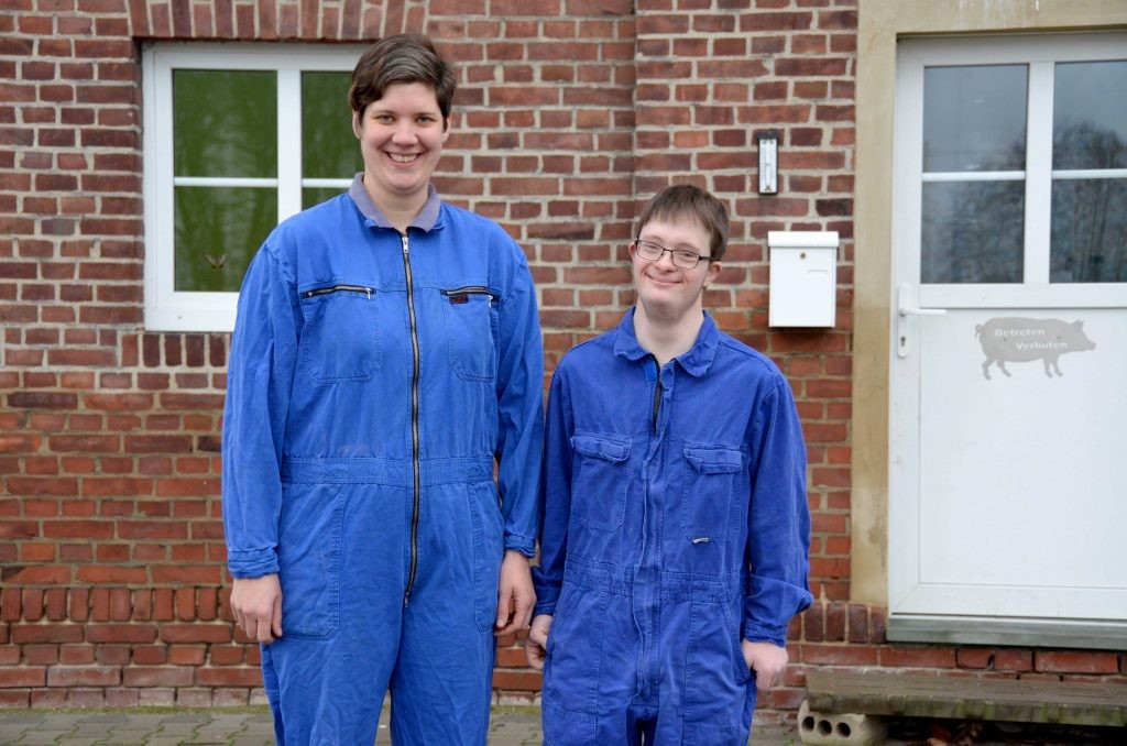 Silke Witte steht neben Tobias Koddebusch vor dem Haus. Beide tragen einen blauen Overall und lächeln in die Kamera.