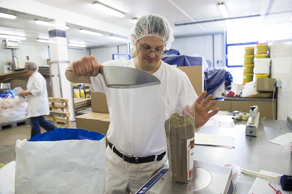 Andŕe Wilbert trägt ein Haarnetz und füllt Gewürze in eine Plastiktüte, die auf einer Waage steht.