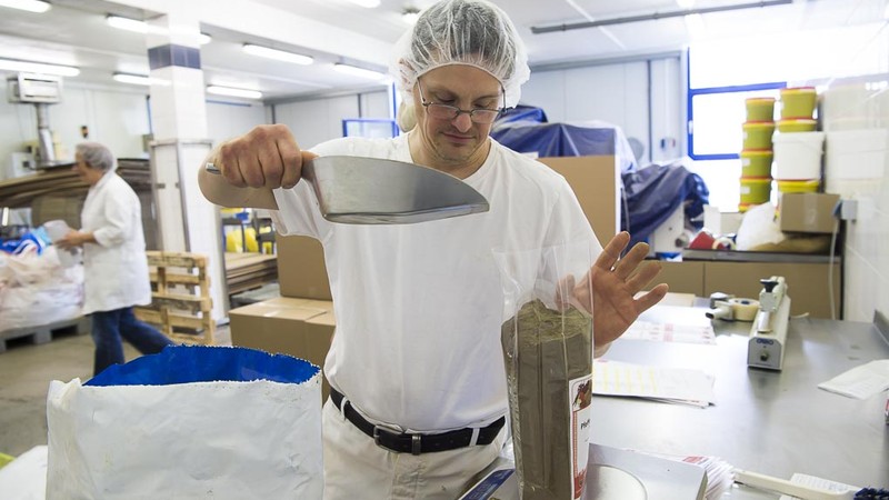 Andŕe Wilbert trägt ein Haarnetz und füllt Gewürze in eine Plastiktüte, die auf einer Waage steht.