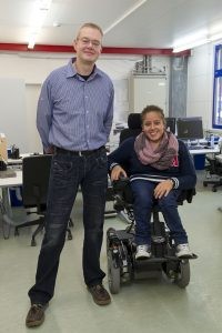 Dirk Fitscher steht neben Rafa Lawah, die in ihrem hohenverstellbaren Rollstuhl sitzt.