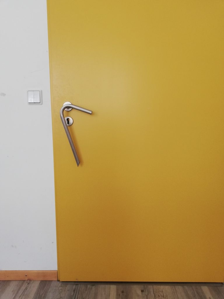 Eine gelbe Tür mit einer nach unten langgezogenen Klinke, die auch kleine Menschen gut erreichen können.