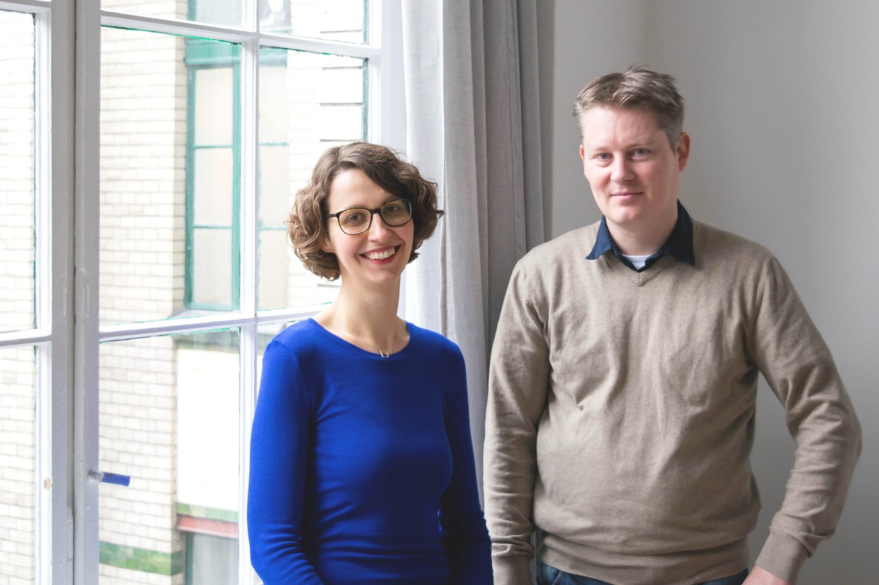 Sally Ollech (links) und René Kuhlemann (rechts) stehen in einem hellen Büro von Diversicon und lächeln in die Kamera.