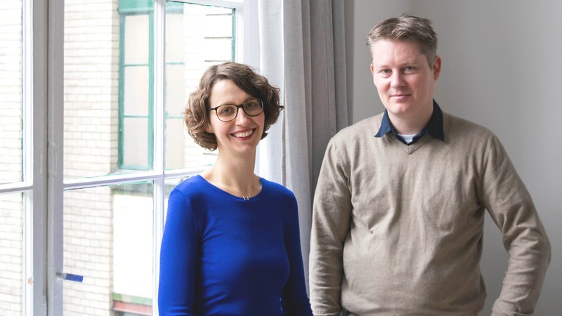 Sally Ollech (links) und René Kuhlemann (rechts) stehen in einem hellen Büro von Diversicon und lächeln in die Kamera.