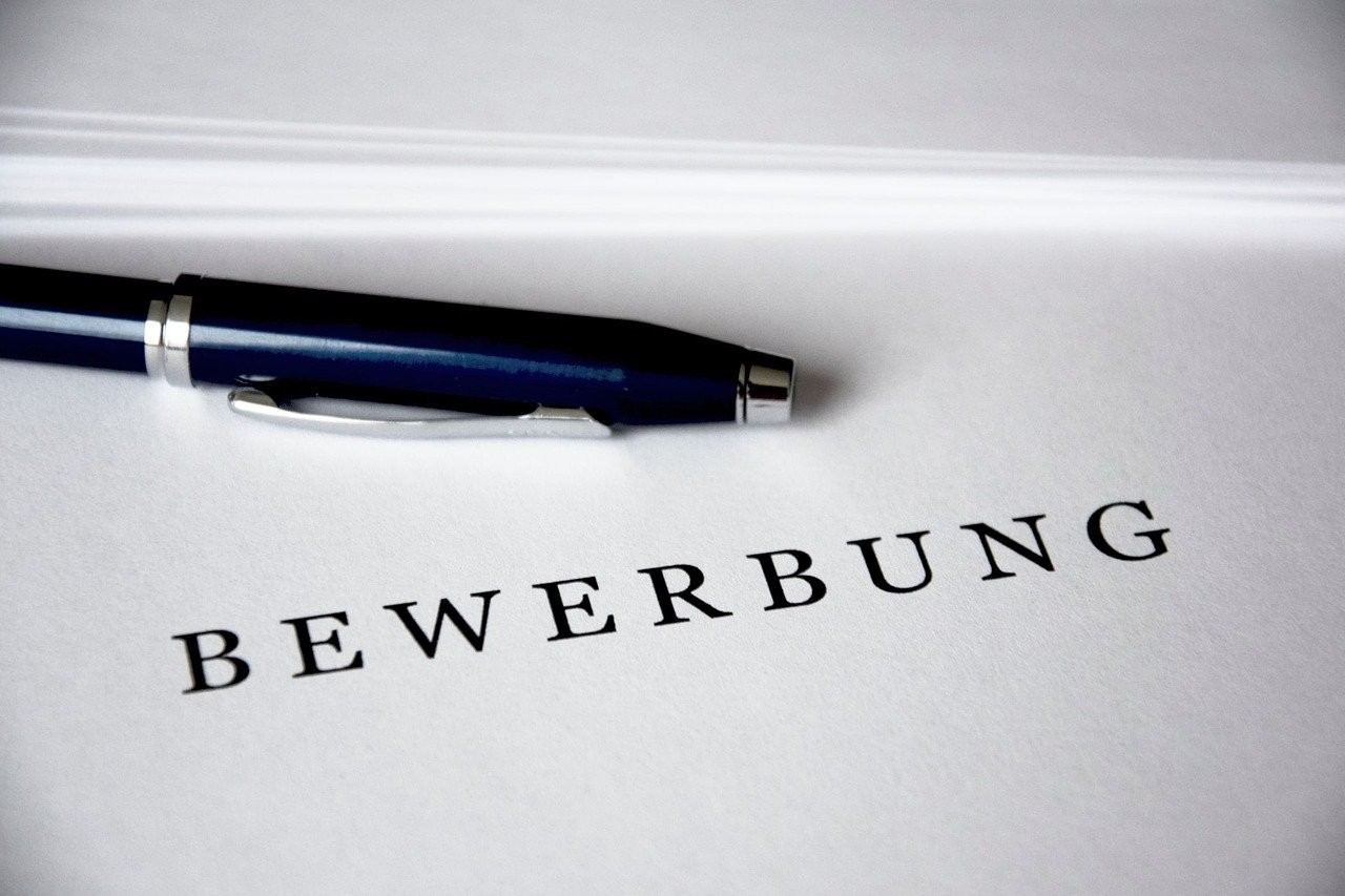 Auf einer weißen Mappe steht das Wort "Bewerbung", darüber liegt ein Kugelschreiber.