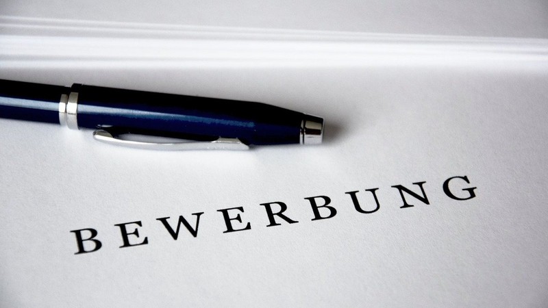 Auf einer weißen Mappe steht das Wort "Bewerbung", darüber liegt ein Kugelschreiber.