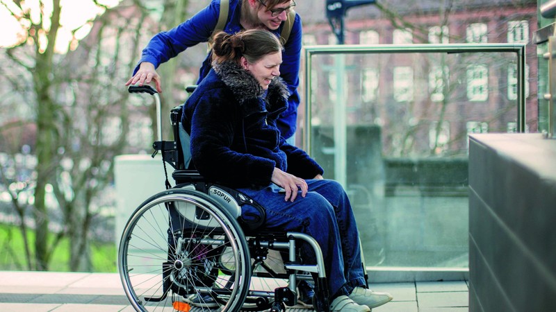 Eine Assistentin begleitet eine junge Frau mit Rollstuhl.