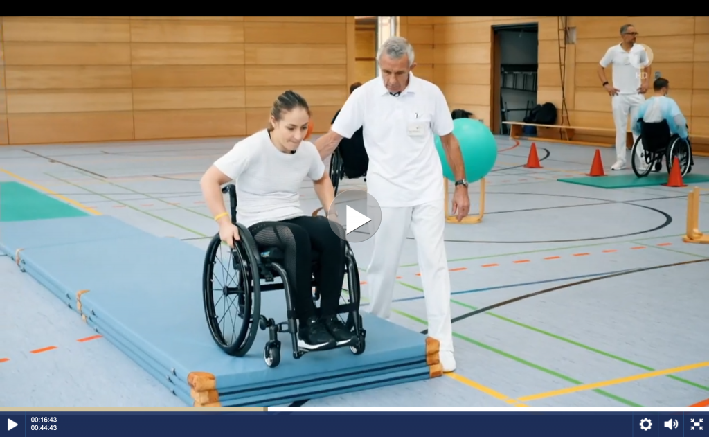 Video-Ausschnitt: Kristina Vogel mit ihrem Trainer beim Rollstuhltraining in einer Turnhalle.