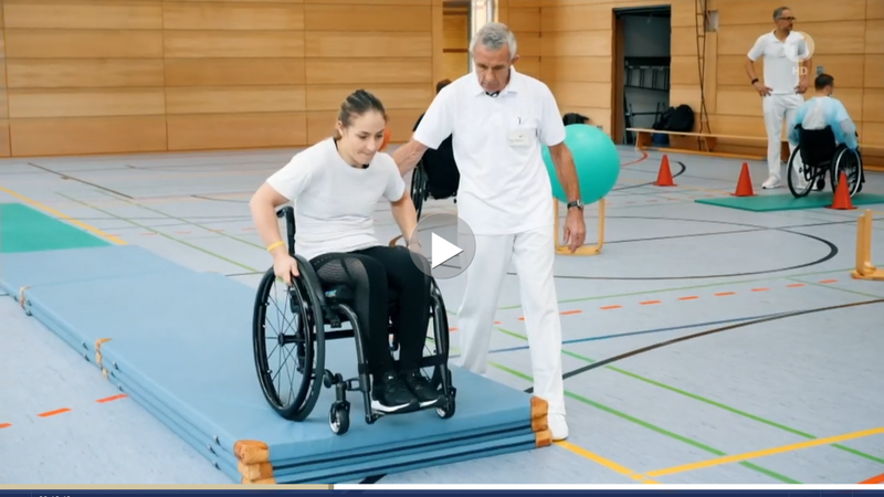 Video-Ausschnitt: Kristina Vogel mit ihrem Trainer beim Rollstuhltraining in einer Turnhalle.