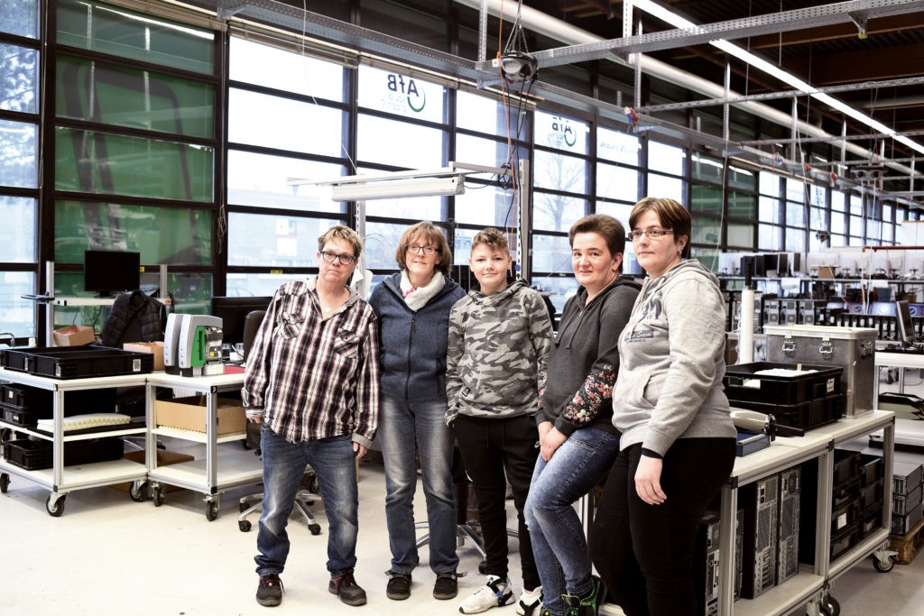 Einige Mitarbeiterinnen und ein junger Praktikant posieren in einer Reihe in der Halle der AfB für die Kamera. Links im Bild ist die Mitarbeiterin Jutta Dieckmann zu sehen.