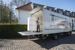 Der Grenzland-Mitarbeiter schiebt einen weißen Wäschecontainer aus dem Lkw auf die Laderampe hinaus.