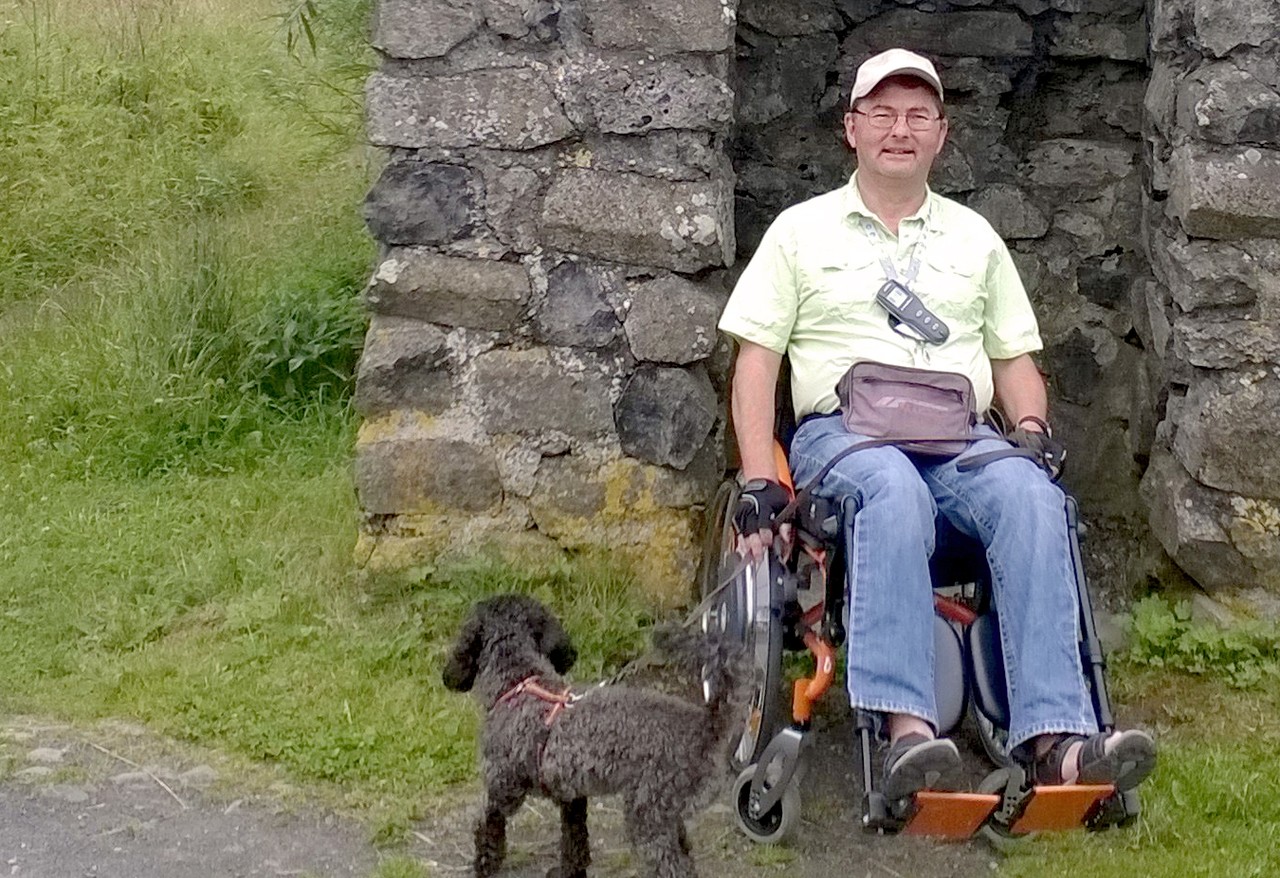 Norbert Sandmann mit Rollstuhl und Hund unterwegs in der Natur.