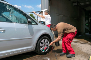 Zwei Mitarbeiter des Servicehauses Stemwede reinigen ein Auto: Einer betätigt einen Hochdruckreiniger, der andere wäscht die Felgen.